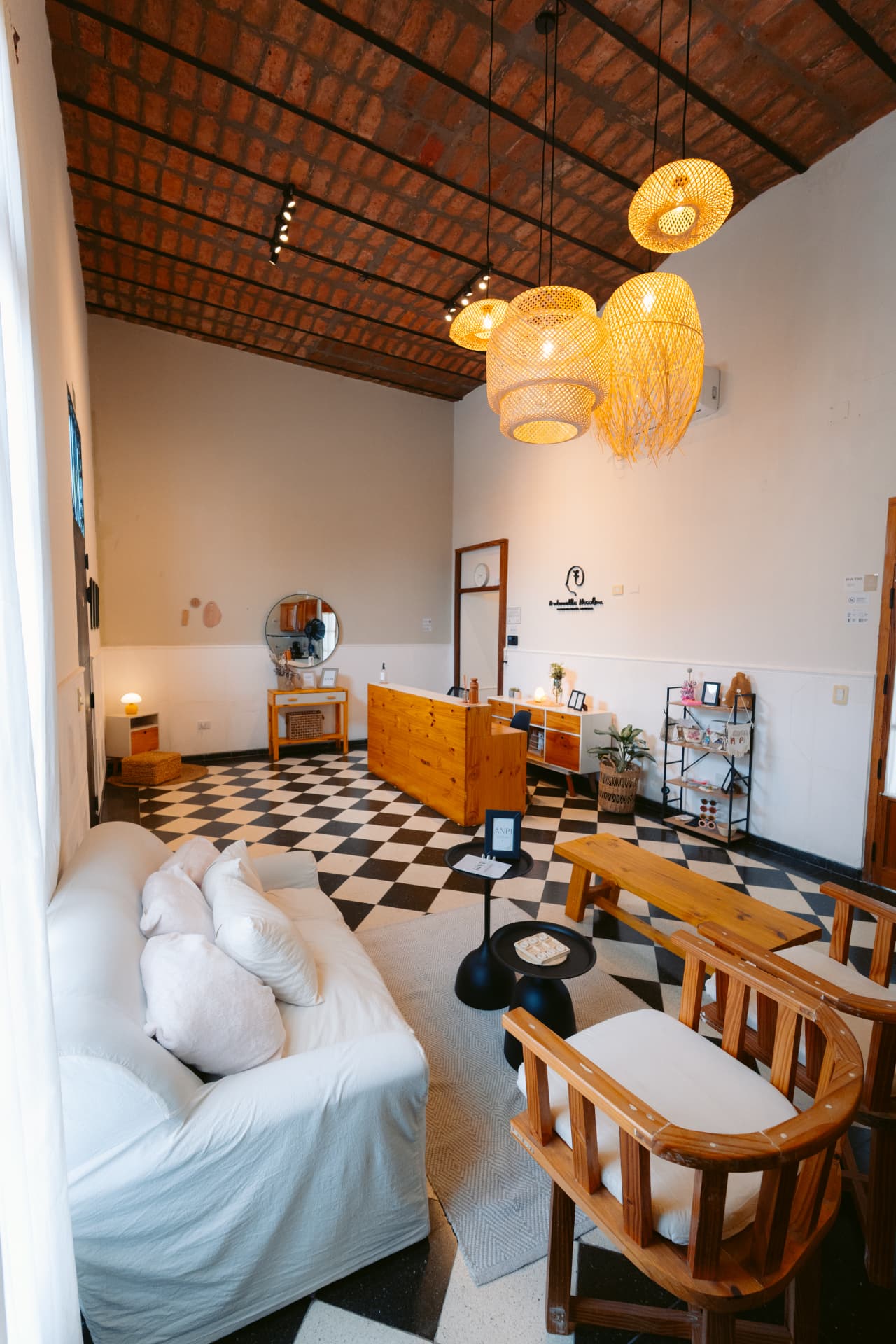 Recepción de Centro ANPI de diseño exclusivo: mostrador de madera, lámparas de fibra natural, techo de ladrillo a la vista y sala de espera con sillones blancos sobre piso damero.