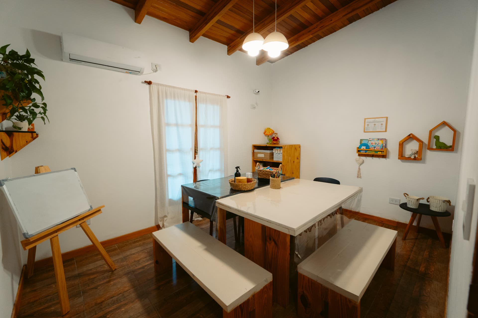 Sala de apoyo escolar de Centro ANPI: mesas de madera con bancos, pizarrón de caballete, estantes con materiales didácticos y luz natural.