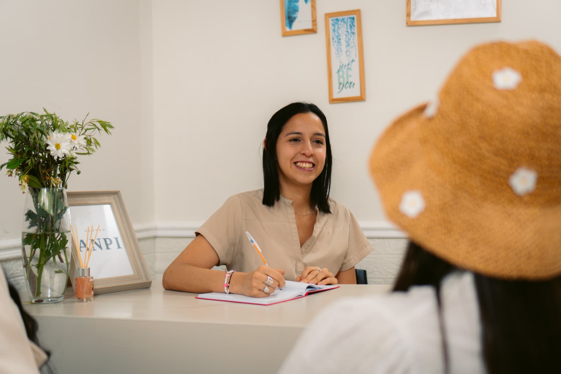 Clara López, Lic. en Kinesiología, sonriendo mientras registra notas en su consultorio en Centro ANPI, con el logo institucional de fondo.