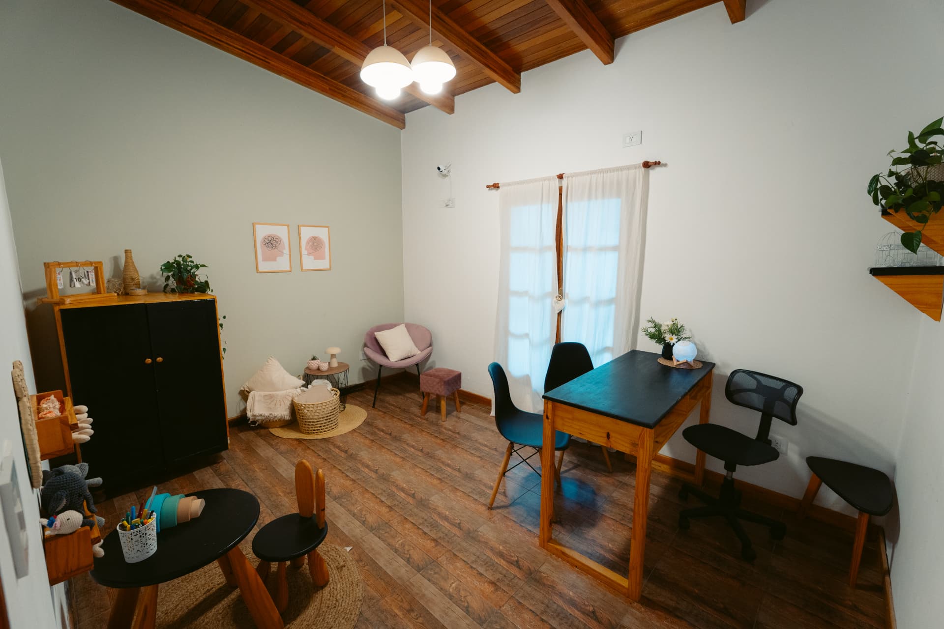 Sala de psicología de Centro ANPI: escritorio de madera con sillas, sillón de lectura con almohadones, cuadros enmarcados y luz natural.