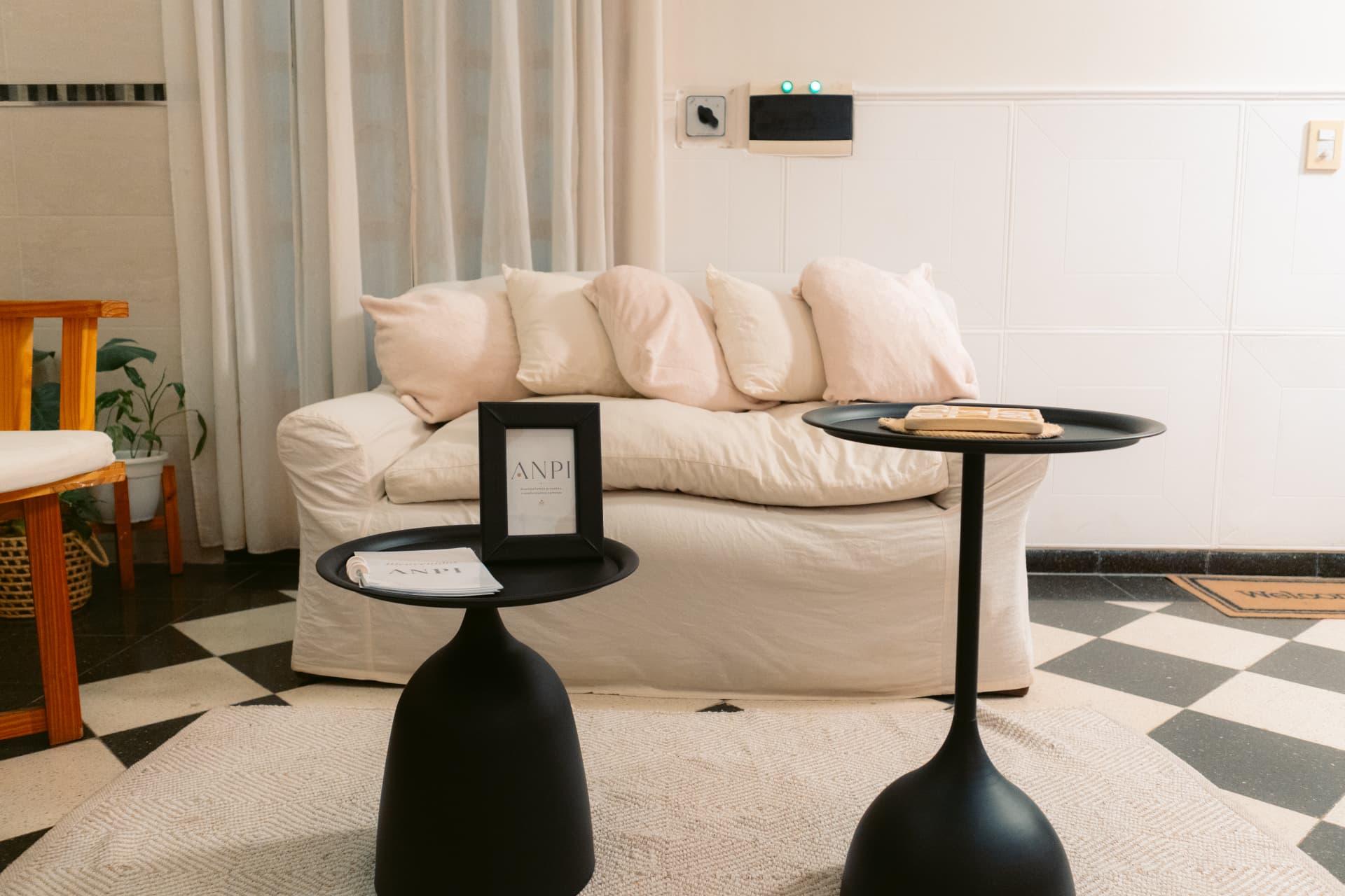 Sala de espera de Centro ANPI: sillón blanco con almohadones suaves, mesas de apoyo negras con material institucional, plantas y piso damero.