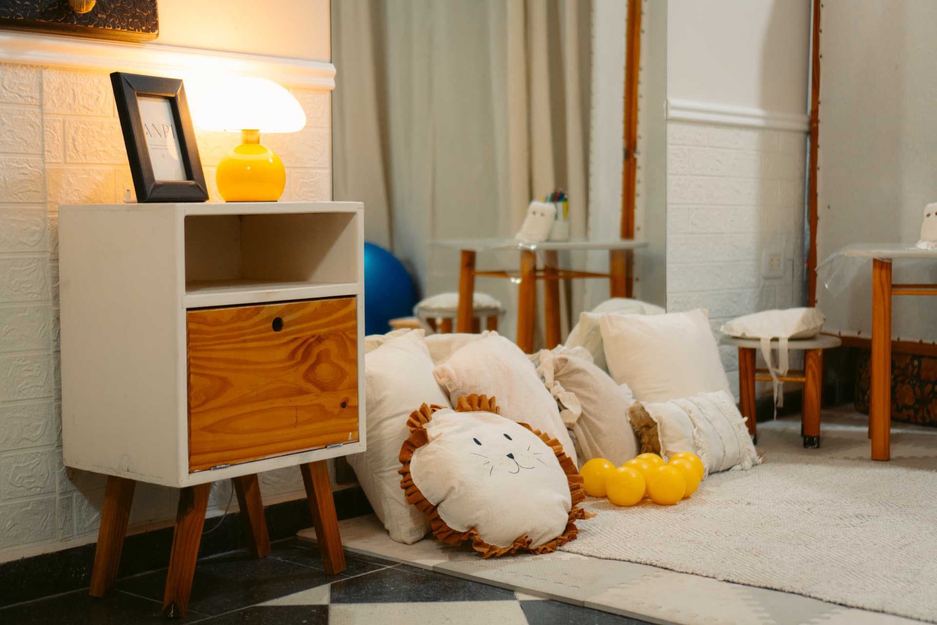 Sala de kinesiología de Centro ANPI: mueble bajo blanco con lámpara y portarretratos del logo, almohadones y pelotas amarillas sobre la alfombra, pelota de pilates azul y pared espejada.